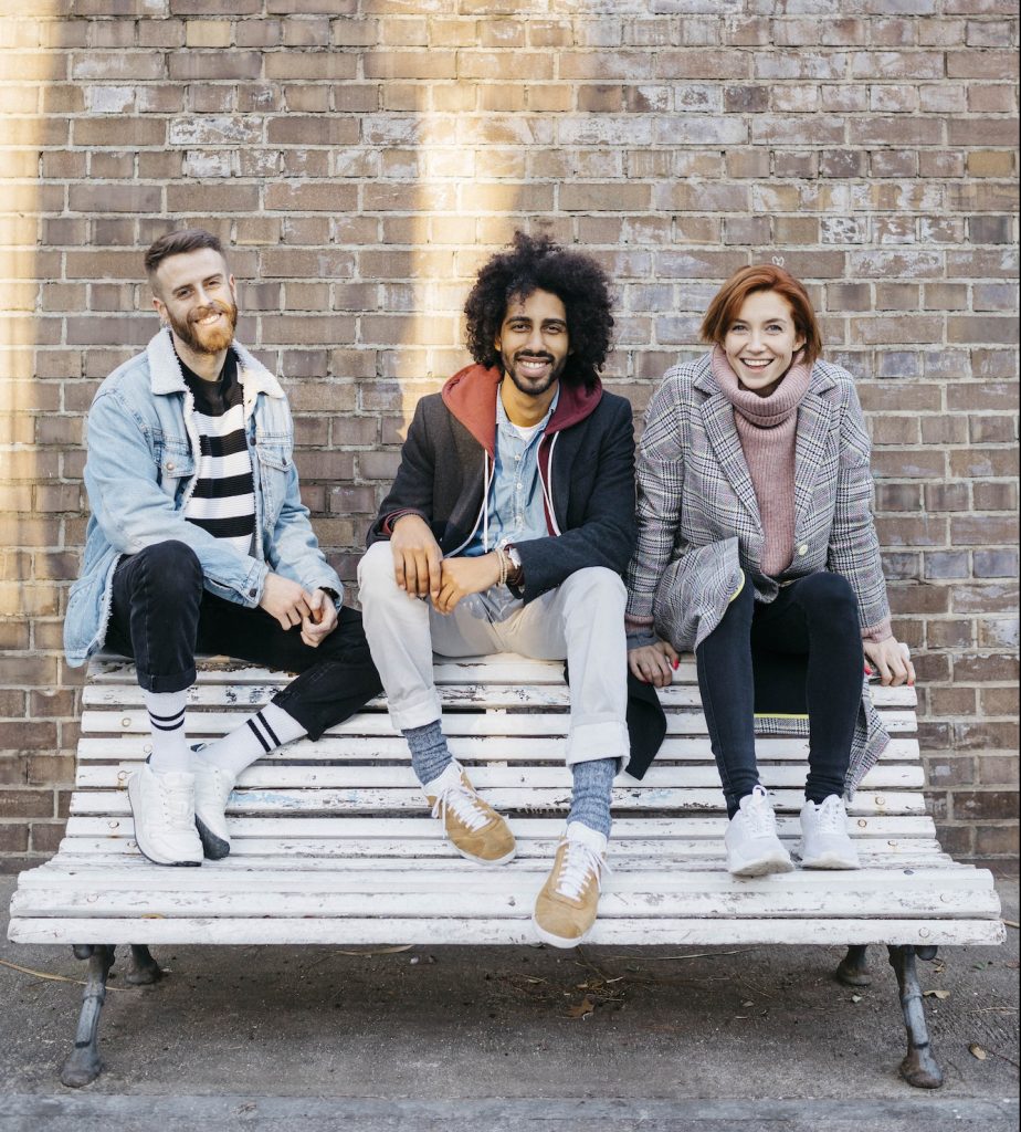Portrait of three happy friends sitting on a bench in front of a brick wall