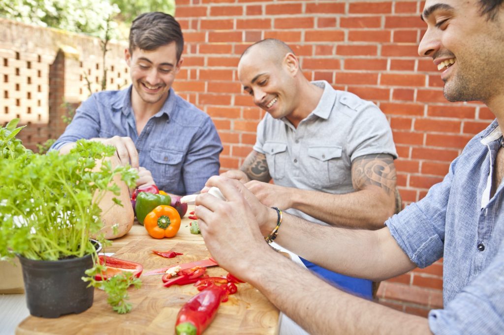 Three male friends laughing and preparing food for garden barbecue